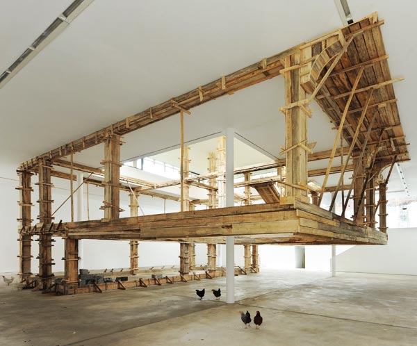 Artikelbild: Die Hohlform eines Einfamilienhauses als kaum kenntliches Ideal einer sicheren Behausung, vorerst nur bewohnt von Hühnern - von Petrit Halilaj im Erdgeschoß der KunstWerke errichtet. - Foto: Uwe Walter