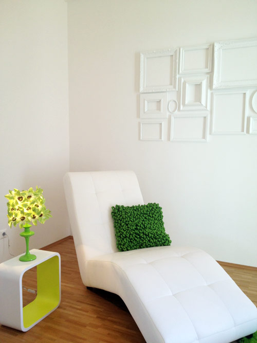 Die Chaiselongue, darüber ein Ensemble aus weißen Bilderrahmen.