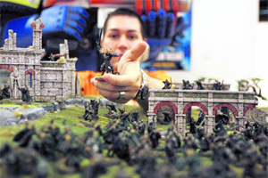 Einer der Spieler im Games Workshop mit einer seiner Figuren aus "Der Herr der Ringe" inmitten eines aufgebauten Schlachtfelds. Was aussieht wie völliges Chaos, ist die Ordnung des Spiels.