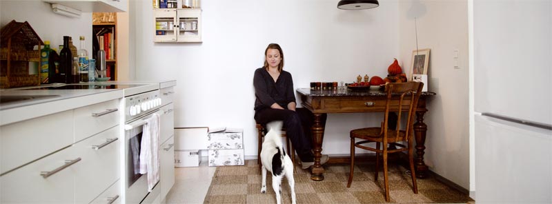 Jutta Ambrositsch und ihr Hund Edgar in der Küche ihrer Wohnung, in der sie mit ihrem Mann, einigen Kisten Wein und lauter verschiedenen Stühlen wohnt. 